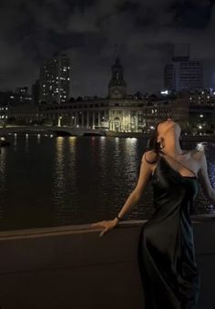 a woman in a black dress leaning on a wall near the water with her eyes closed