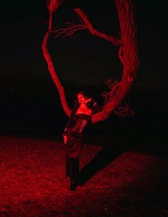 a woman standing in front of a tree with red light on her face and arms