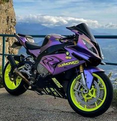 a purple and yellow motorcycle parked on the side of a road next to a cliff