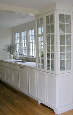 a kitchen with white cabinets and wood flooring next to a window filled with windows