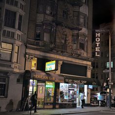 an empty street at night with people walking on the sidewalk and buildings in the background