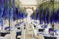 tables and chairs are set up with blue flowers hanging from the ceiling in an elegant setting