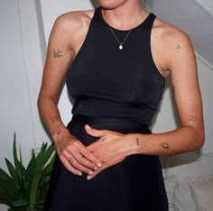 a woman with tattoos on her arm standing next to a potted plant and wearing a black dress