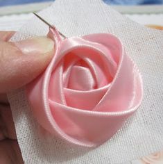 a person is stitching fabric with a sewing needle and pink rose on the piece of cloth