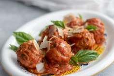 meatballs covered in marinara sauce and herbs on a white plate with yellow trim