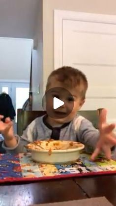 a little boy sitting at a table with a pie in front of him