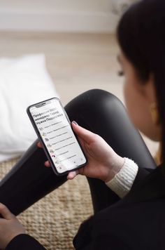 a woman is sitting on the floor looking at her cell phone while holding it in her hand