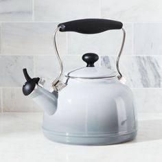 a white tea kettle sitting on top of a counter next to a marble wall and tile backsplash