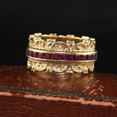 two gold rings with red stones on them sitting on top of a wooden table next to a black background