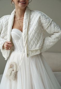 a woman in a white dress and jacket with pearls on her necklace, posing for the camera