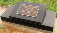 a black box with a plaque on it sitting in the grass next to some dirt