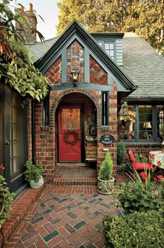 a brick house with a red door surrounded by greenery and potted plants on either side