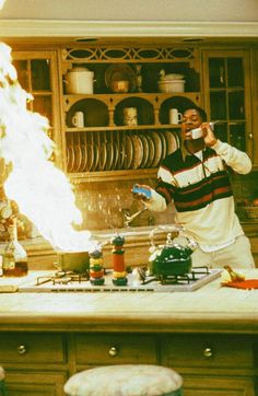 a man standing in a kitchen next to a stove top oven with flames coming out of it