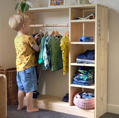 a little boy standing in front of a closet with clothes hanging on the rail and shelves