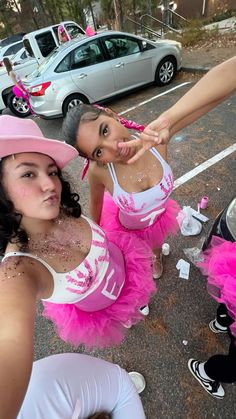 two women dressed in pink and white standing next to each other on the side of a road