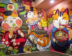 a colorful mural on the side of a building with cats eating out of bowls and holding chopsticks