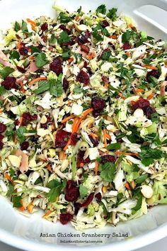 a salad with cranberries, celery, carrots and lettuce in a white bowl