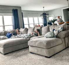 two people laying on the couches in a living room with blue curtains and large windows