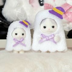 two white stuffed animals with purple hats and bows on their heads sitting next to each other