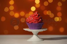 a cupcake with red frosting and sprinkles sits on a cake plate