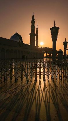 the sun is setting behind two tall buildings with spires in the background and shadows on the ground