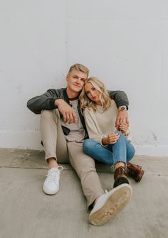 a man and woman sitting on the ground next to each other with their arms around each other