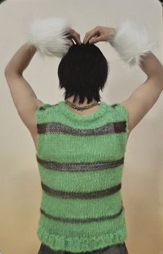 a man with his hands on his head wearing a green sweater and furry white gloves