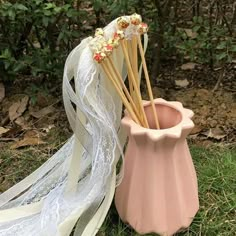 a pink vase with some sticks sticking out of it sitting in the grass next to a white veil