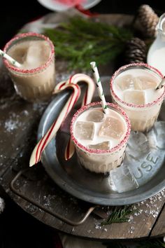 two glasses filled with ice and candy canes on top of a metal platter