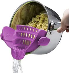 a purple strainer filled with pasta being held by someone's hand over the sink