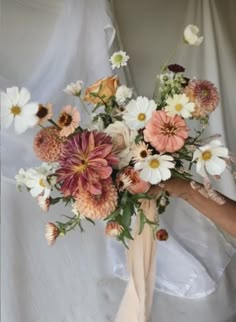 a woman holding a bouquet of flowers in her hand on a white cloth covered background