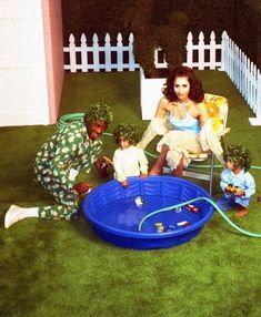 a woman sitting in a chair next to two small children and an infant on the ground