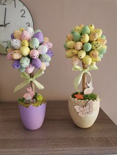 two small vases with fake eggs in them on a table next to a clock