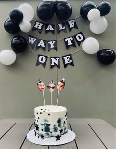 a birthday cake with black and white balloons on the wall behind it that says half way to one