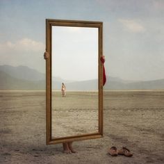 a person standing in the middle of a desert holding up a mirror to their face