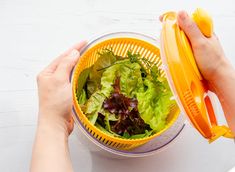 two hands holding a salad in a strainer on top of a white countertop