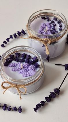 two jars filled with purple flowers on top of a white table next to twine string