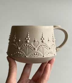 a hand holding a white ceramic cup in it's right hand, with beaded designs on the outside