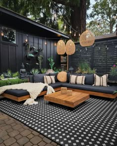 an outdoor living room with black and white rugs, wooden furniture and hanging lights