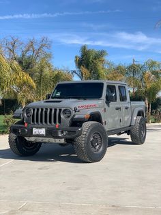 a gray jeep parked in a parking lot with palm trees and blue sky behind it