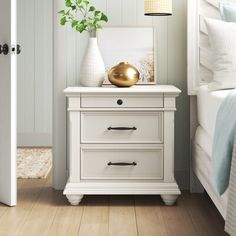 a white nightstand with a gold ball on it next to a bed in a bedroom