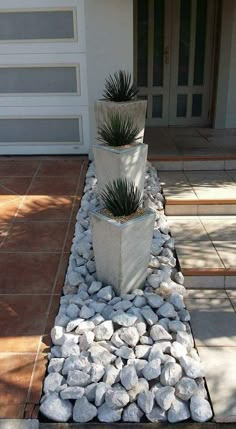 two large planters sitting on top of rocks in front of a house with a door