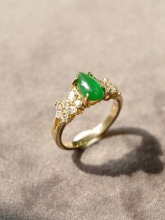 a gold ring with a green stone and three diamonds on the side, sitting on a gray surface