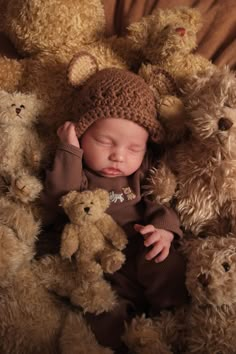 a baby is sleeping among many teddy bears and wearing a knitted hat with his hands on his head