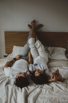 two people laying on a bed with white sheets