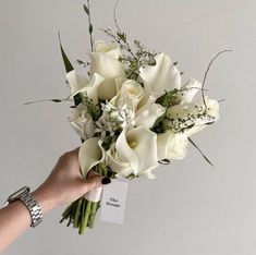 a bouquet of white flowers being held by a woman's hand with a tag on it