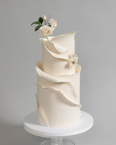 a three tiered white wedding cake with flowers on the top and bottom, sitting on a pedestal