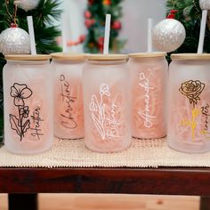 four glass jars with writing on them are sitting on a table next to christmas decorations