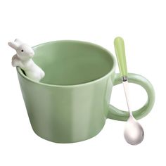 a green cup with a spoon in it and a white bunny figurine on top