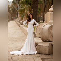 a woman in a long sleeved wedding dress poses for a photo on the sidewalk